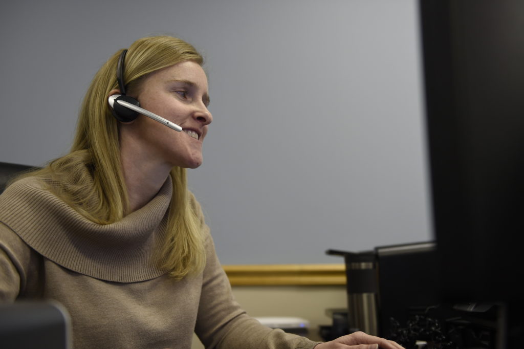Photo of employee smiling and talking on a headset while sitting at a desk in the office at IOB